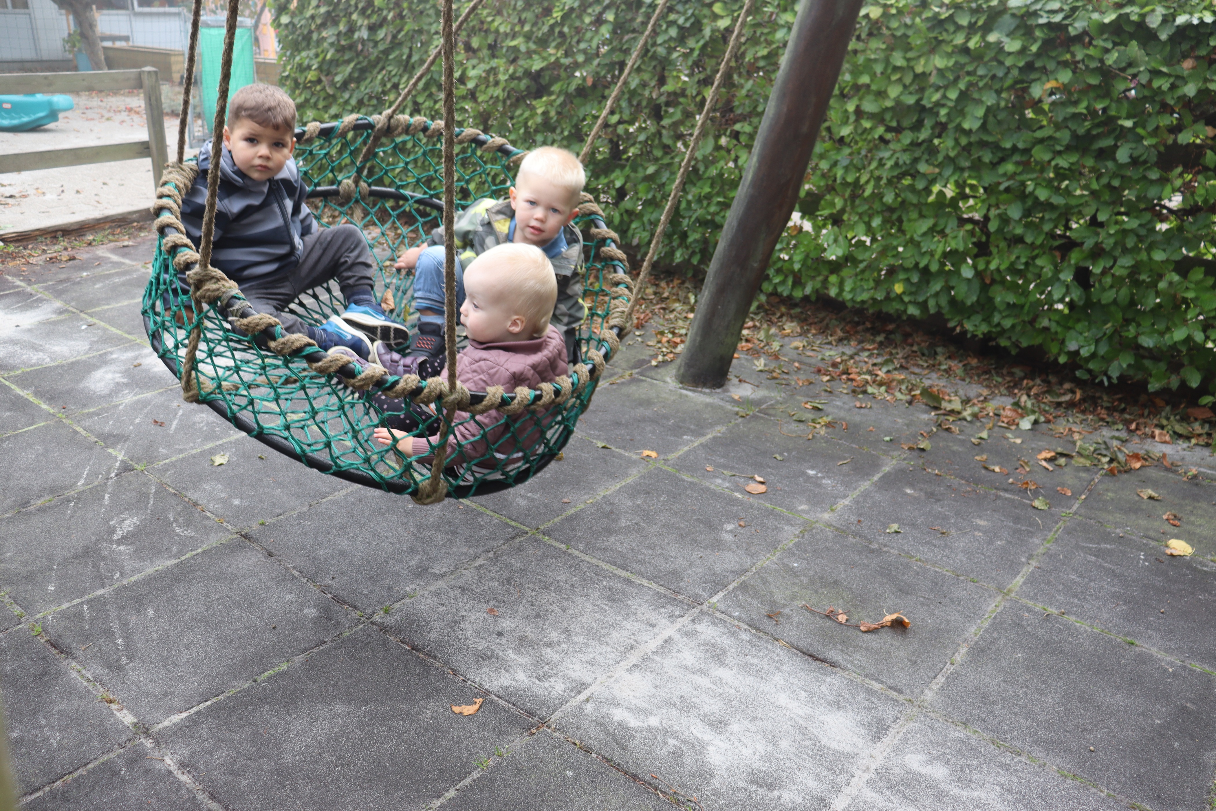 Tre børn sidder i en hængegynge, imens der gynges
